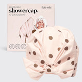 Pink shower cap with brown polka dots and packaging on a light gray background