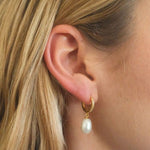 Woman wearing FYB gold huggie hoop earrings with clear CZ accents and pearl drops