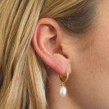 Woman wearing FYB gold huggie hoop earrings with clear CZ accents and pearl drops