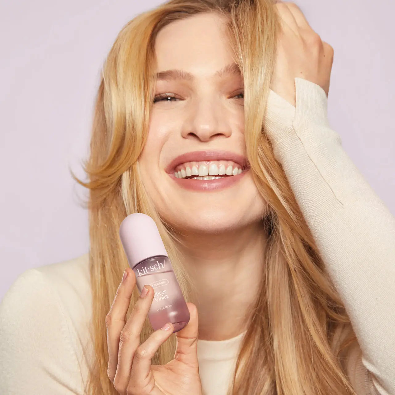 Woman holding a bottle of Kitsch's Sheer Violet Hair Perfume with a blurred background