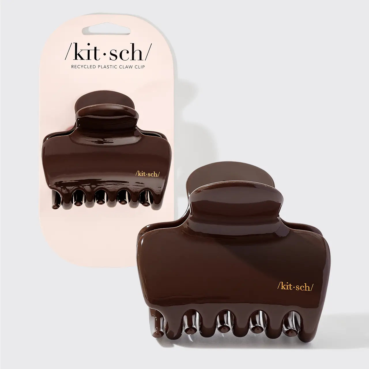 Two dark brown glossy claw hair clips shown on a light gray background, with one clipped to a pale pink Kit·sch card and one loose in front. The Kit·sch brand name is visible on both the card and the clips. 