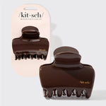 Two dark brown glossy claw hair clips shown on a light gray background, with one clipped to a pale pink Kit·sch card and one loose in front. The Kit·sch brand name is visible on both the card and the clips. 