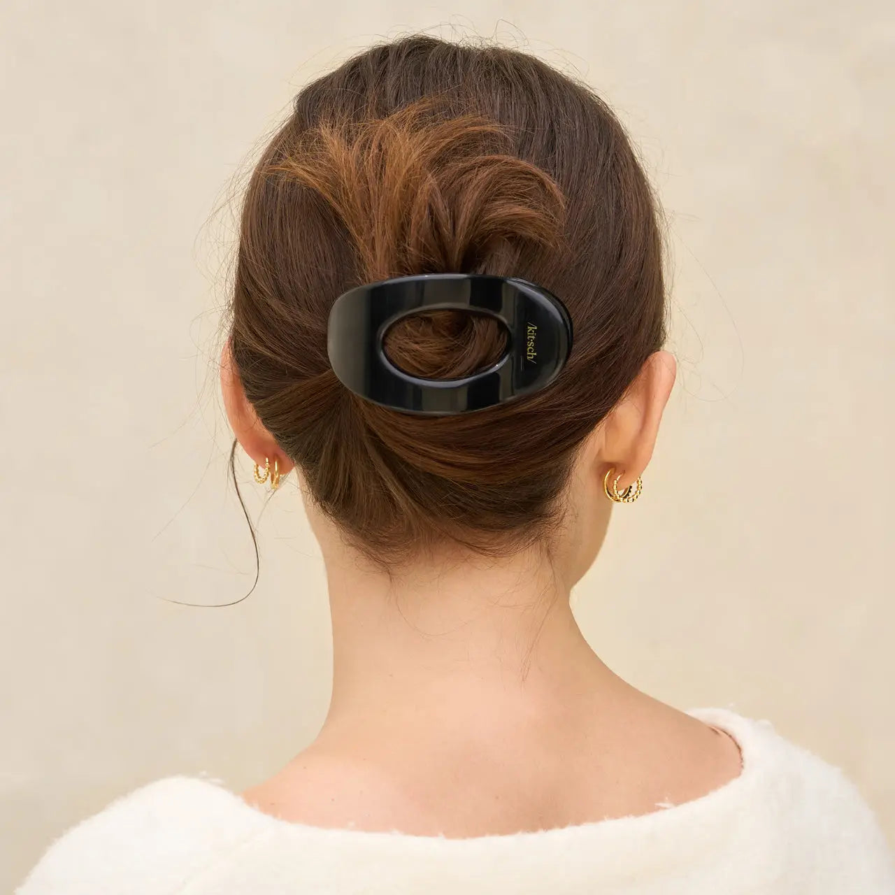 Person with a hair bun holding a black hair clip against a beige background