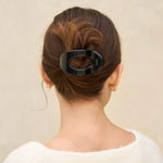 Person with a hair bun holding a black hair clip against a beige background