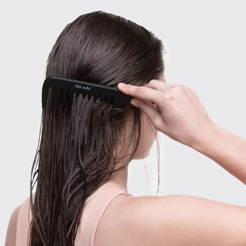 Person using a black Detangle Wide Tooth Comb on their hair with a plain background