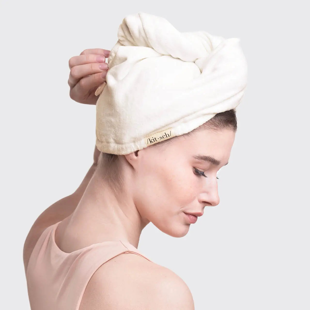 Woman wearing a white towel on her head with a visible brand logo against a light gray background