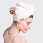 Woman wearing a white towel on her head with a visible brand logo against a light gray background