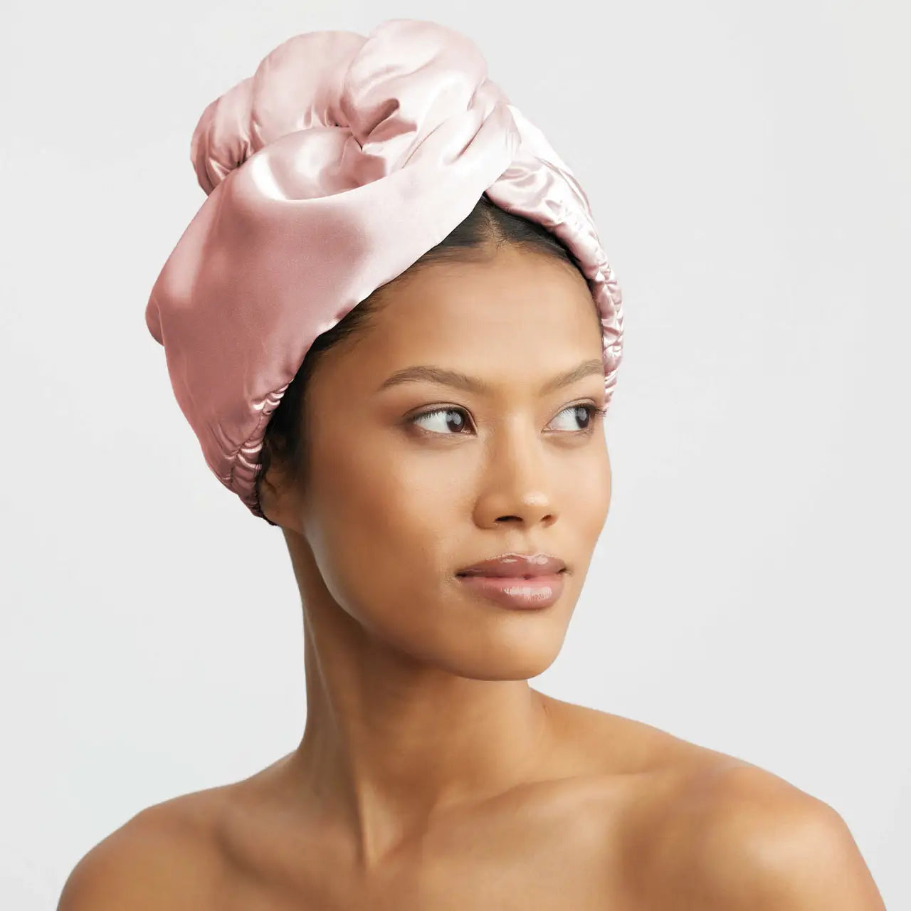 Woman wearing a pink satin hair wrap on a plain background