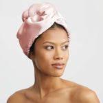 Woman wearing a pink satin hair wrap on a plain background