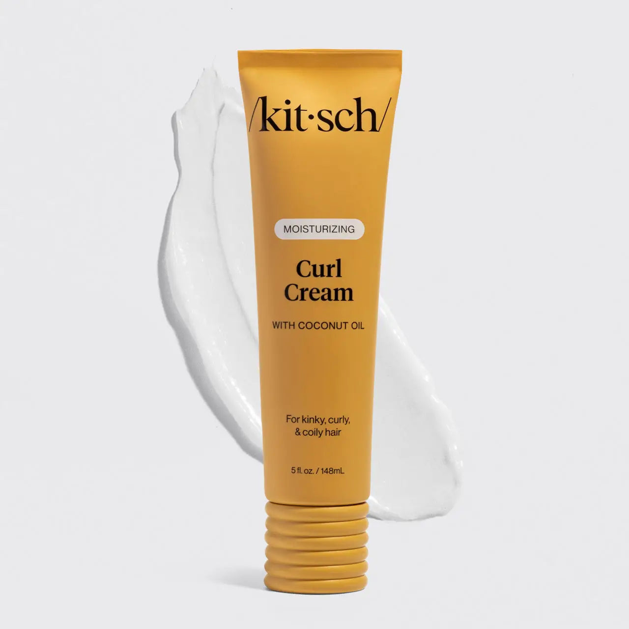 A squeeze tube of Kitsch Moisturizing Curl Cream with coconut oil, shown in a golden yellow color with a white cream smear behind it on a light gray background.