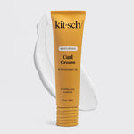 A squeeze tube of Kitsch Moisturizing Curl Cream with coconut oil, shown in a golden yellow color with a white cream smear behind it on a light gray background.