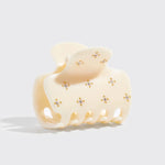 Cream-colored hair claw with decorative elements on a light gray background from Nespoli Jewelers.