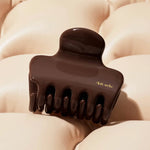 Brown hair clip with 'kitsch' branding on a beige textured background from Nespoli Jewelers.