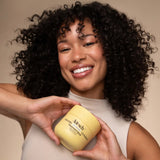 Woman holding a jar of Kitsch's hair mask against a beige background