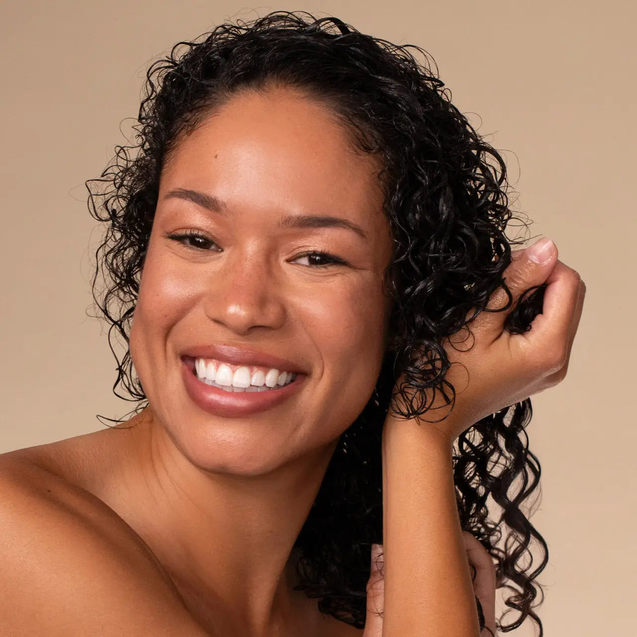 Woman using Kitsch Moisturizing Curl Cream smiling against a beige background