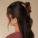 A woman shown in side profile wearing a brown translucent claw hair clip holding part of her dark hair up against a plain beige background.