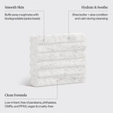 A white textured cleansing bar with black speckles, shown on a light gray background with callout text describing its benefits: Smooth Skin, Hydrate & Soothe, and Clean Formula.
