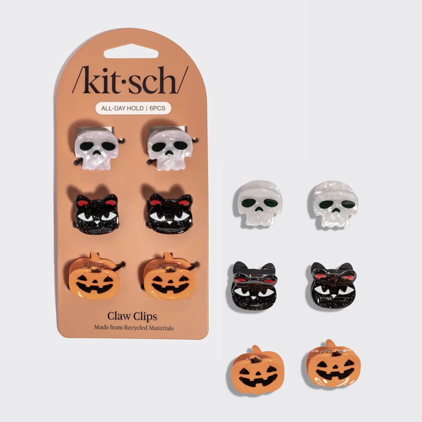 Six Halloween-themed claw clips from the brand kit·sch, displayed on their peach-colored cardboard backing card alongside three loose clips. The set includes skull, black cat, and orange pumpkin designs.