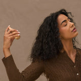 Woman holding Kitsch Rustic Vanilla perfume  against a brown background