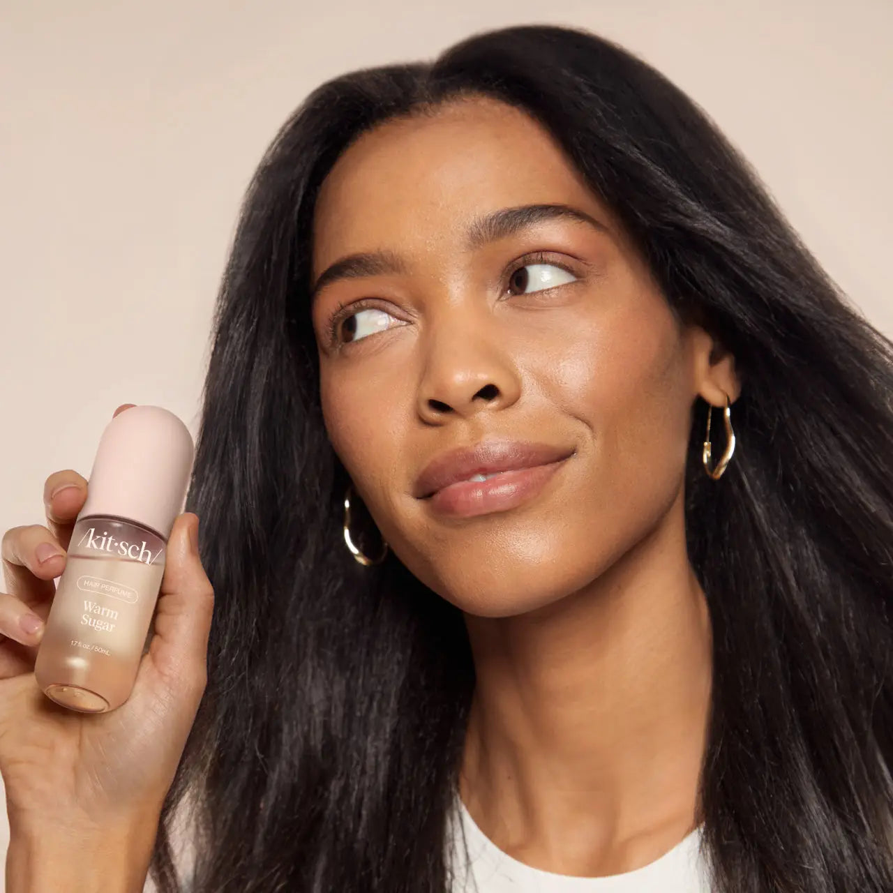 Woman holding a Kitsch Warm Sugar Hair Perfume with a neutral background