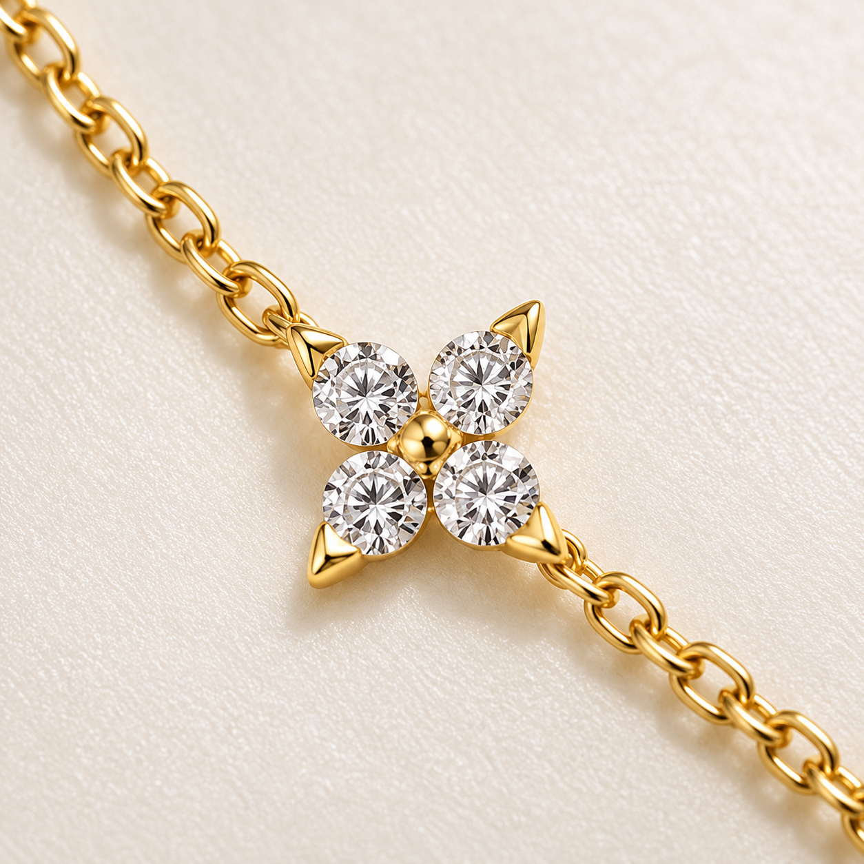 A close-up of a gold chain bracelet featuring a four-flower clover motif with four round-cut clear gemstones in a gold setting, displayed on a textured off-white background.