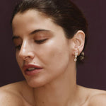 Close-up of woman wearing gold clear CZ dangle earrings featuring three graduated stone shapes.