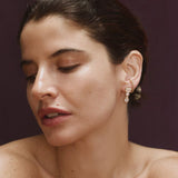 Close-up of woman wearing gold clear CZ dangle earrings featuring three graduated stone shapes.