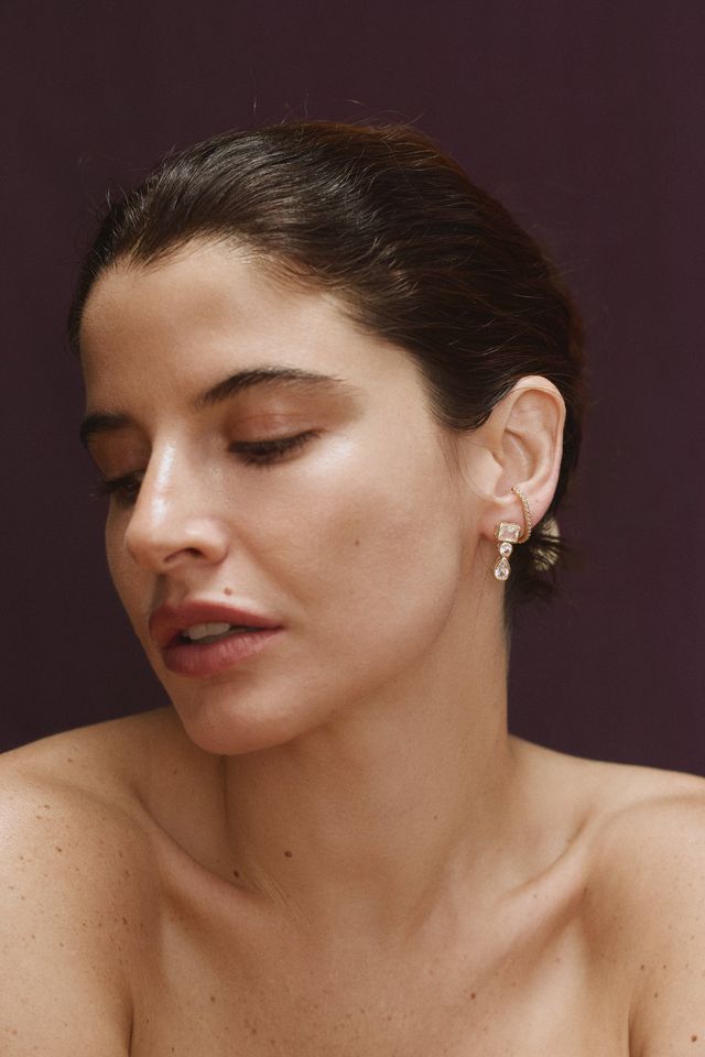 Close-up of woman wearing gold clear CZ dangle earrings featuring three graduated stone shapes.