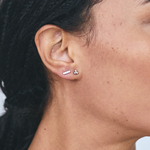 Woman wearing silver three-bead cluster stud earrings paired with a slim bar stud.