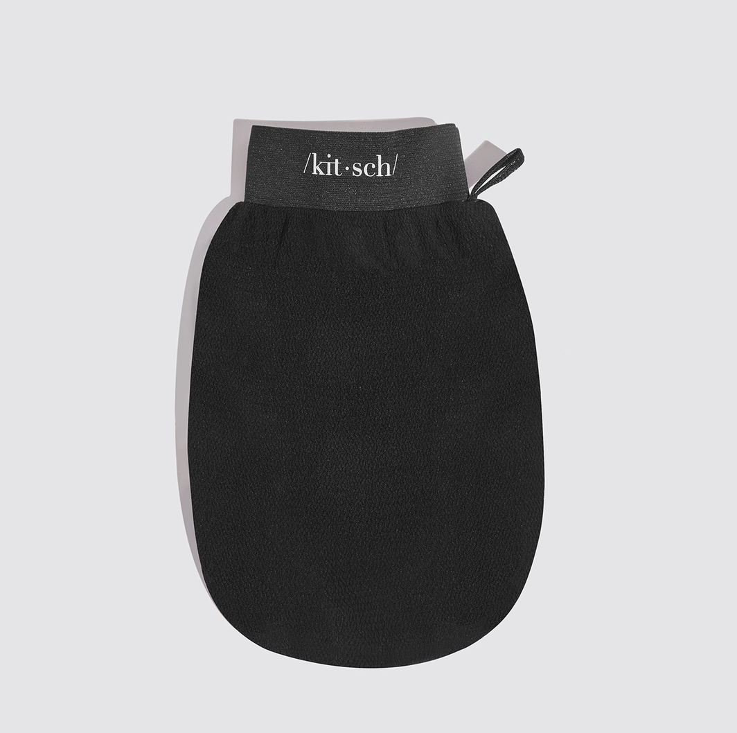 A black silicone hand scrubber mitt with a gray elastic wrist strap featuring the white printed brand name '/kit·sch/' and a small black pull tab, shown on a light gray background.