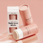 Kit-sch Flyaway Taming Hairwax Stick shown with its white retail box and two pink cylindrical stick containers on a soft pink studio background.