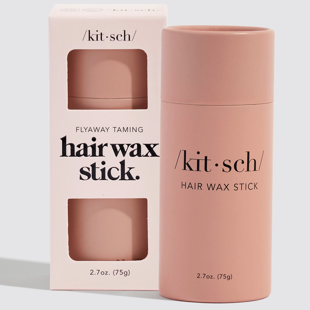 Kit Sch Flyaway Taming Hair Wax Stick in a dusty pink cylindrical container next to its matching light pink packaging box, on a clean light gray background.