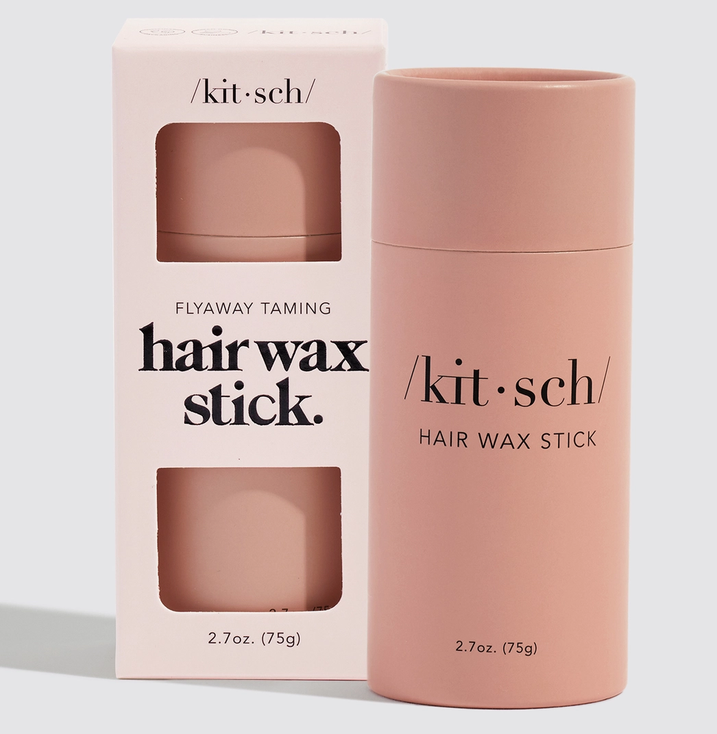 Kit Sch Flyaway Taming Hair Wax Stick in a dusty pink cylindrical container next to its matching light pink packaging box, on a clean light gray background.