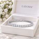 A silver-toned tennis bracelet with clear round stones, displayed inside an open white LAFONN jewelry box on a light marble surface with blurred white flowers in the background.