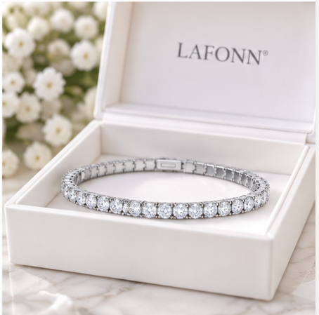 A silver-toned tennis bracelet with clear round stones, displayed inside an open white LAFONN jewelry box on a light marble surface with blurred white flowers in the background.