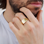 Man wearing a Brosway INK gold signet ring with a brushed geometric face and polished gold finish.