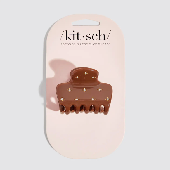 A brown recycled plastic claw clip with small gold star embellishments, mounted on a light pink cardboard hanger card with the brand name 'kit-sch' printed at the top.