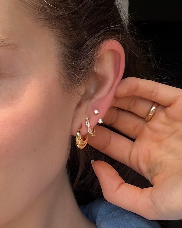 Woman wearing gold FYB double CZ stud earrings as part of a layered ear stack.