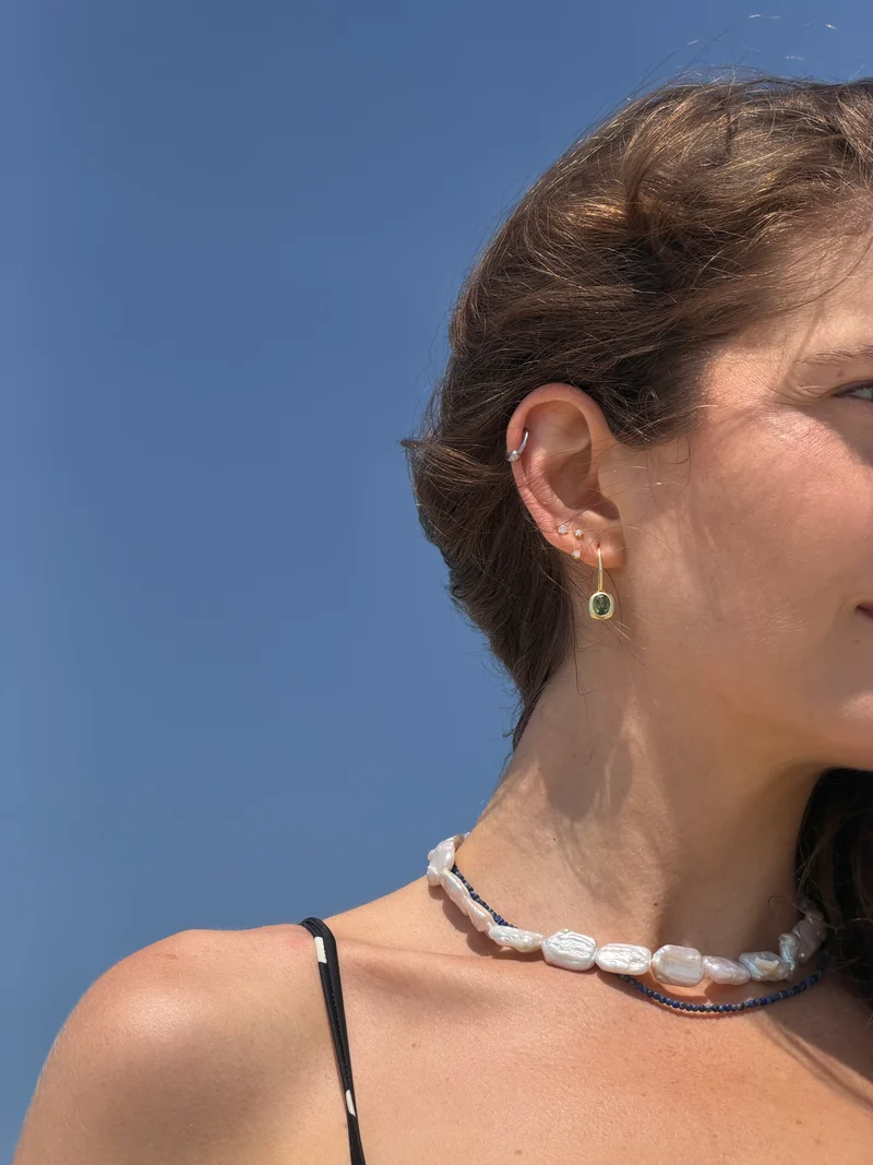 Woman wearing gold olive green stone dangle earrings as part of a layered ear stack.