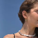 Woman wearing gold olive green stone dangle earrings as part of a layered ear stack.