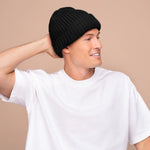 Man wearing a black knit beanie and white t-shirt against a beige background