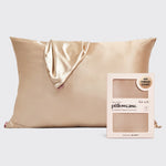 A champagne gold satin pillowcase with a matching satin tie-back corner, shown next to its light pink packaging box labeled 'kit:sch pillowcase' on a light gray background.