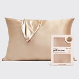 A champagne gold satin pillowcase with a matching satin tie-back corner, shown next to its light pink packaging box labeled 'kit:sch pillowcase' on a light gray background.