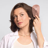 Woman brushing her hair with a Kitsch Detangling Flexi Brush  against a light gray background