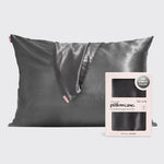 A dark gray satin pillowcase with a matching satin slipcover draped over the front, shown next to its light pink packaging box on a light gray background.