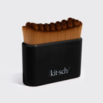 A black rectangular brush holder with the KitSch logo, holding a row of thick brown bristle makeup brushes, photographed on a light gray background.