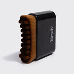 A Kit-sch hand brush with brown bristles and a black handle, standing upright on a light gray background.