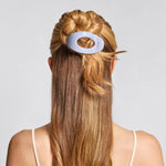Person with long blonde hair wearing a white hair tie against a light gray background