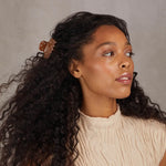 Woman with curly hair wearing a beige sweater against a neutral background