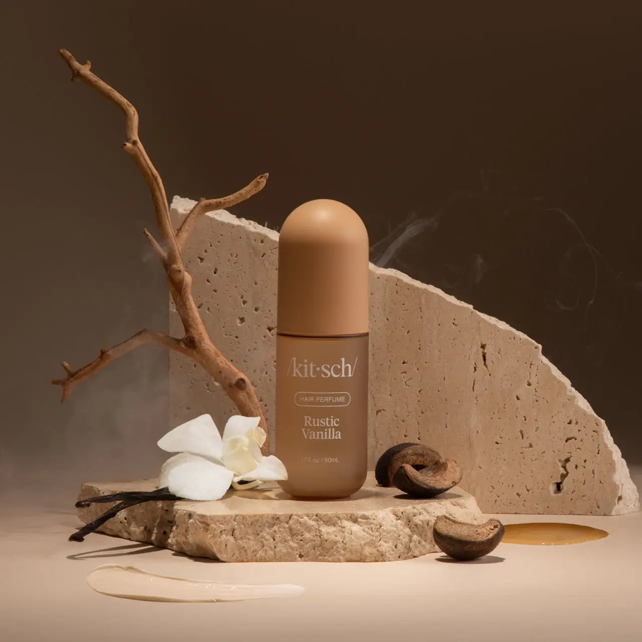 Kit-sch Rustic Vanilla perfume bottle with vanilla beans and flowers on a stone surface.